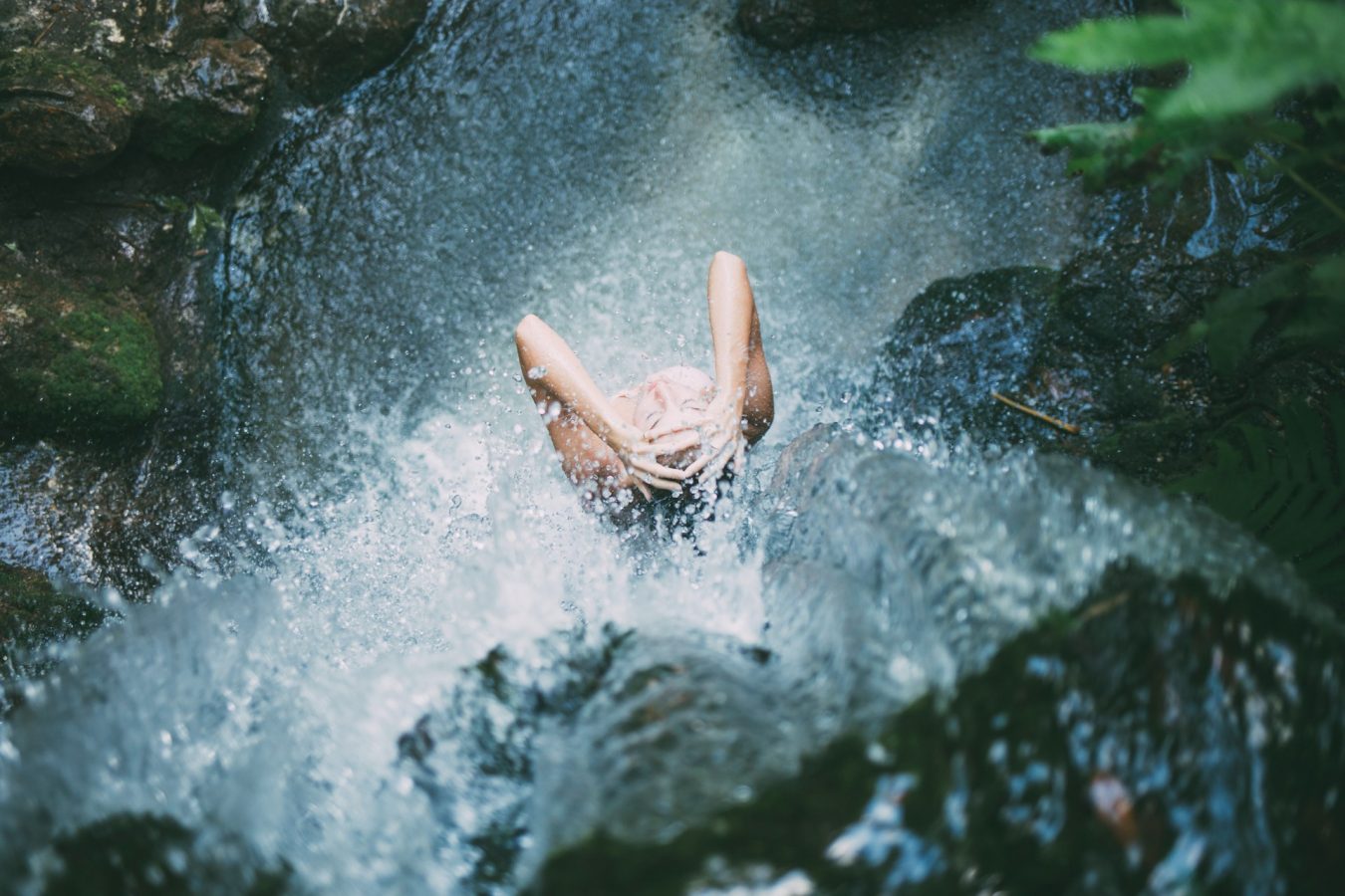 woman bathing below waterfalls during daytime